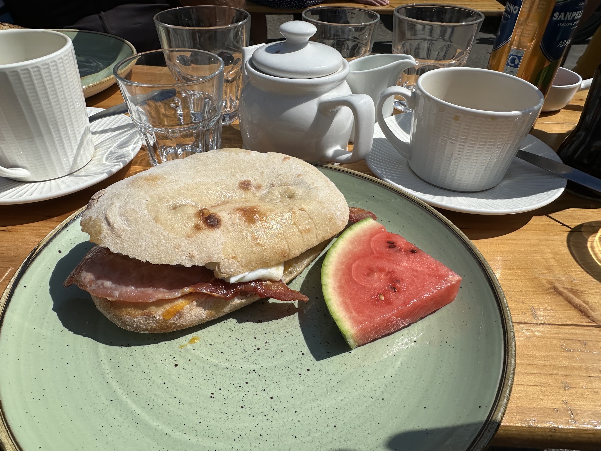 Breakfast bap, a pot of tea and a cup on a sunny outdoor table